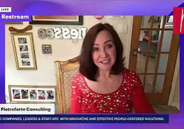 Woman in a dress sitting on a chair in front of a wall adorned with photo frames and a door