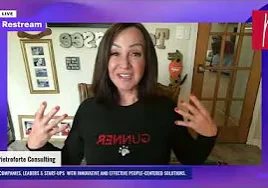 Woman in a shirt on a video call, with a wall behind her adorned with photo frames and other items