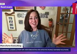 Woman in a shirt talking on a video call, with a wall behind her adorned with photo frames
