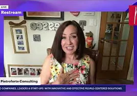 Woman in a floral dress on a TV screen, with a wall behind her adorned with photo frames
